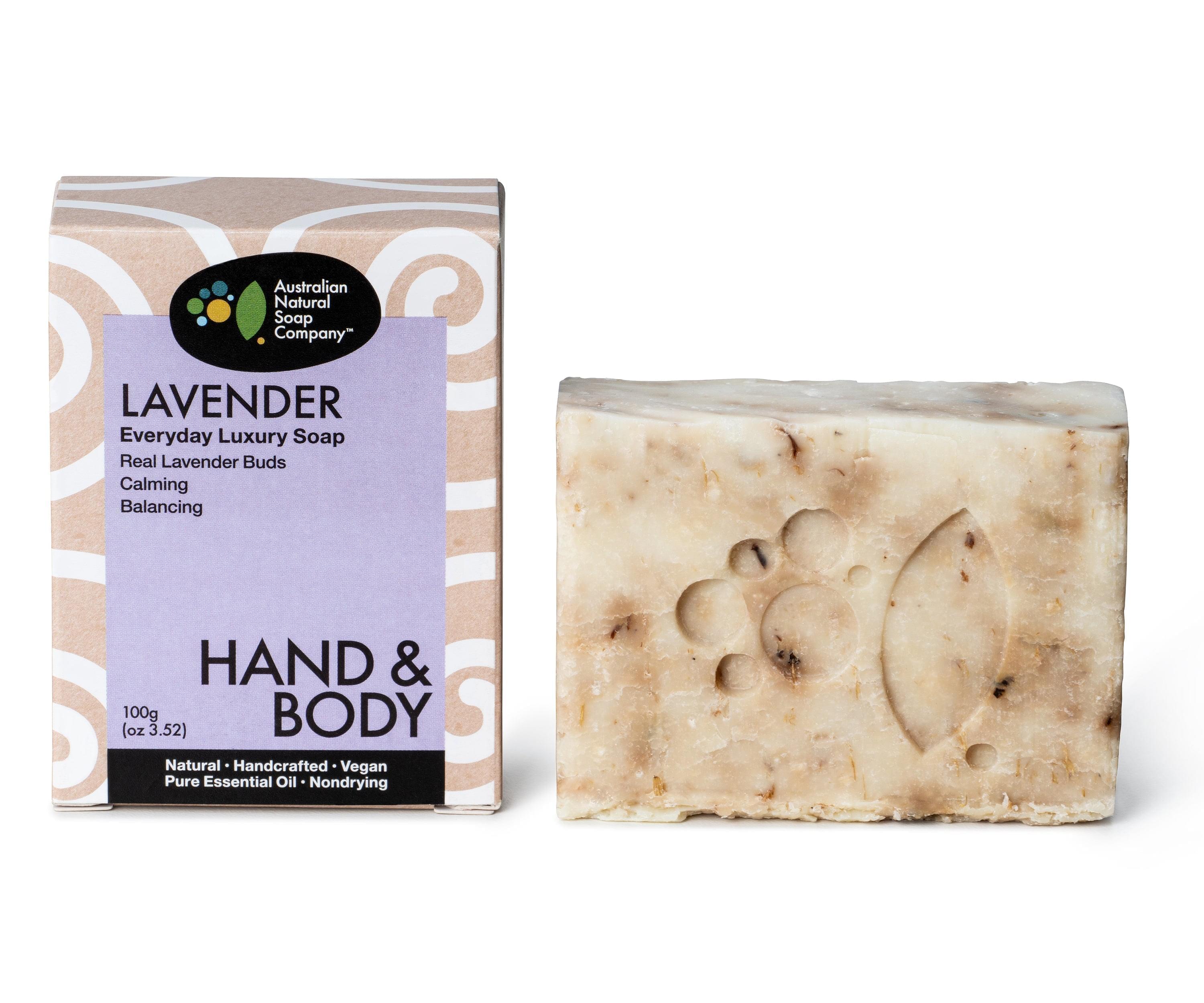 Image of a Lavender soap box featuring a light purple color scheme with a pattern surrounding the purple area. The front of the box clearly states the type of soap and highlights its uses. next to the box is a raw soap bar with specks of lavender buds within it