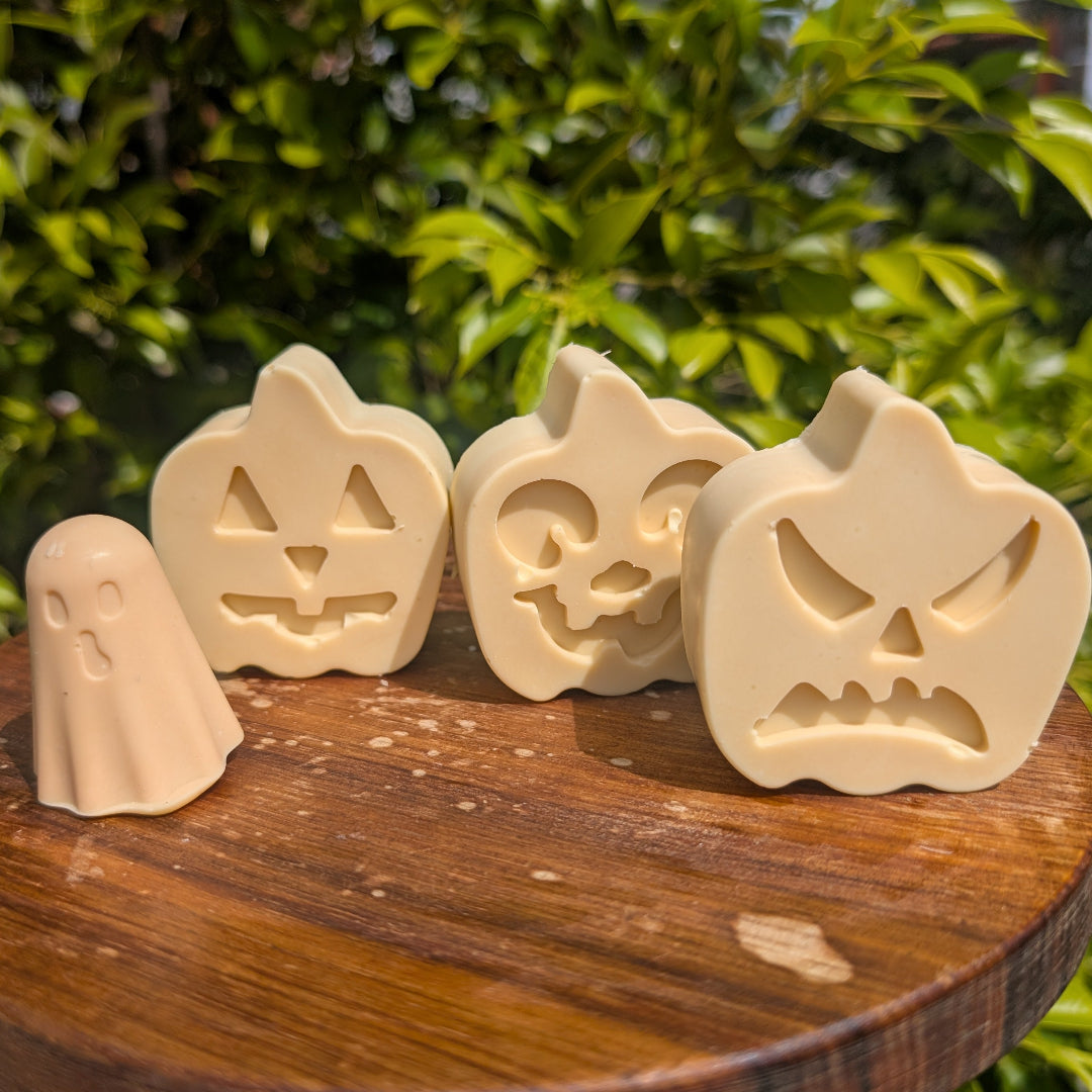 Set of Halloween-themed soap bars on a wooden stand with green foliage in the background